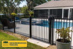 A black metal fence surrounds a backyard swimming pool and raised spa in front of a screened porch.
