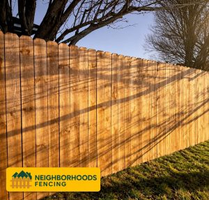 A wooden privacy fence casts tree shadows with grass along the base.